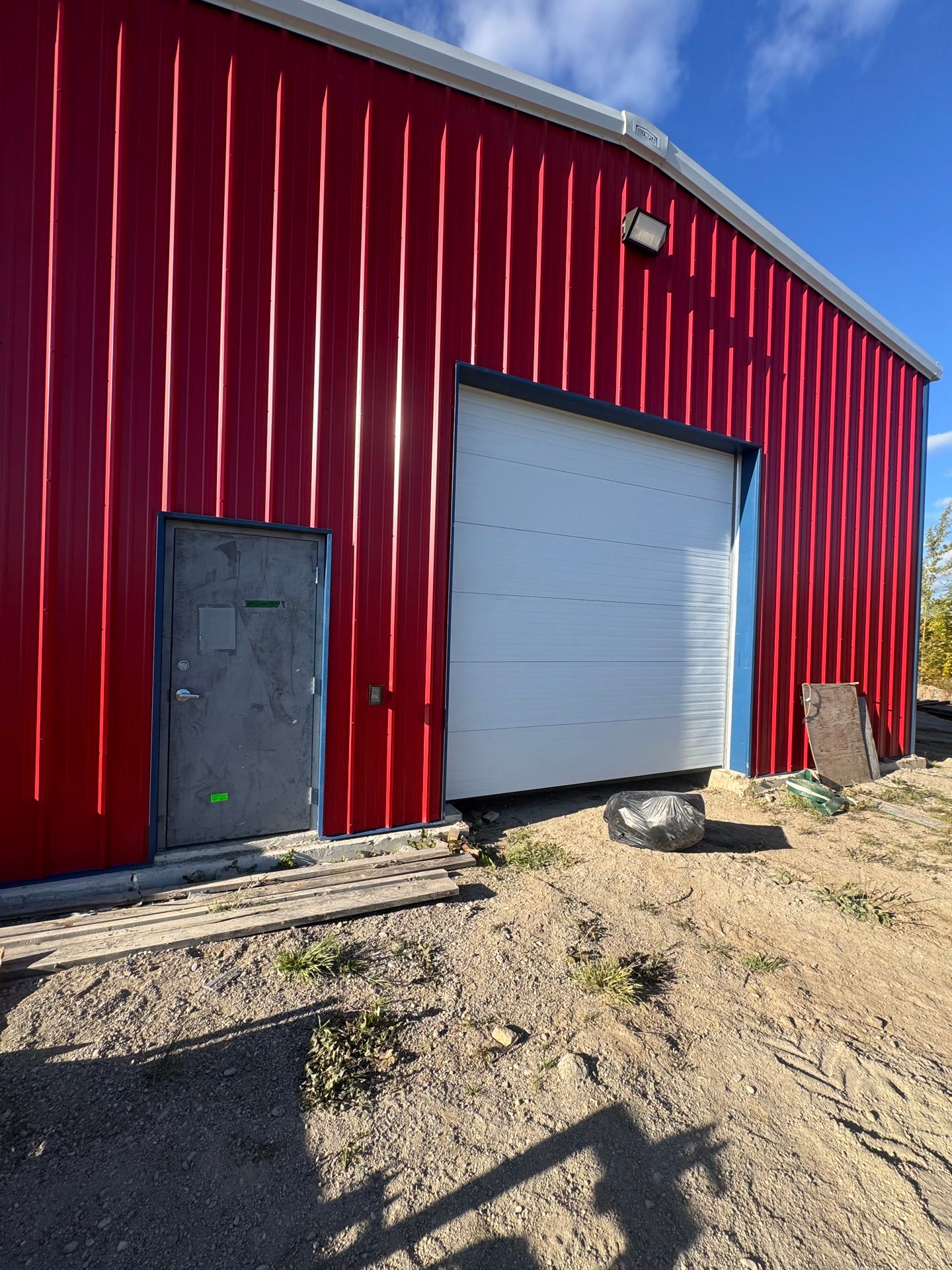 A red steel building with a white overhead door and a service door, under a clear blue sky.