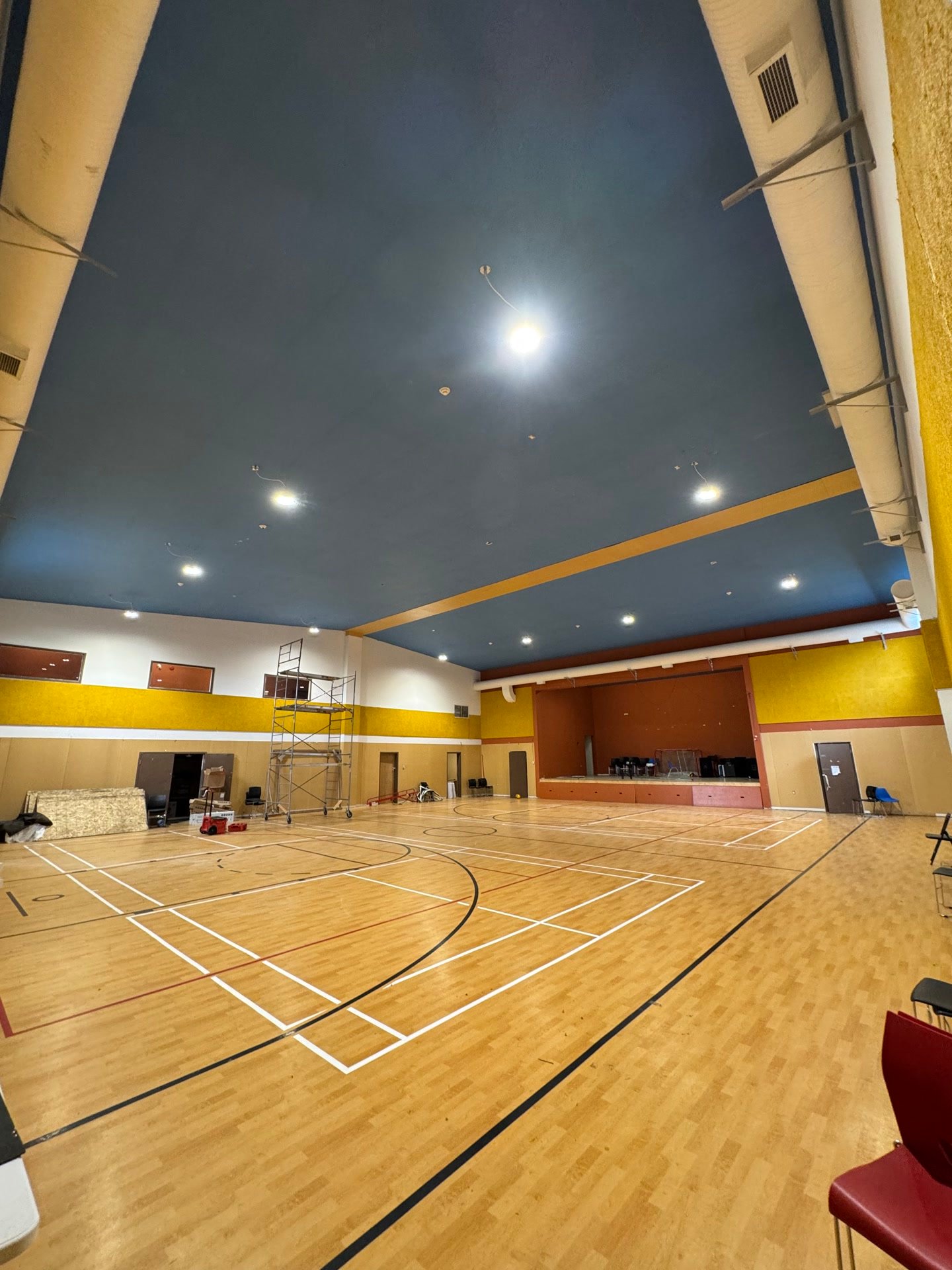 The interior of a finished community hall, hardwood floor laid and the ceiling lights on.