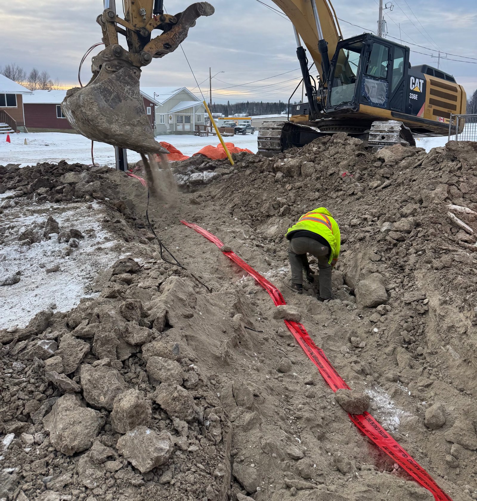 An excavator opening a trench in frozen ground with cable being laid in, low winter light.